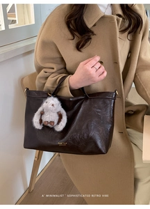 Detail of vintage brown leather tote bag with plush rabbit charm and brand logo