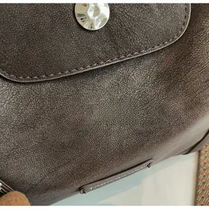 Detail of dark brown lychee texture leather with silver metal hardware and logo patch