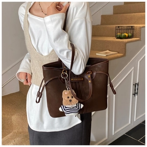 Détail d'un grand sac cabas marron foncé avec plaque logo et breloque ours en peluche