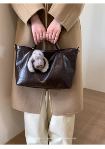 Close-up of deep brown glossy tote bag with gold logo and plush rabbit pendant detail
