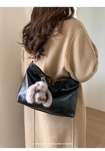 Detail of black glossy leather tote bag with gold hardware and plush rabbit charm