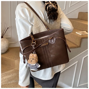 Detailed close-up of dark brown tote bag with vintage badge and cute plush bear accessory