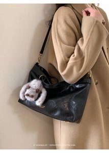 Detail of vintage black tote bag with gold logo, leather texture, and cute plush charm