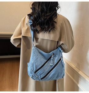 Detail of light blue washed denim hobo bag with diagonal zippers and soft wide strap