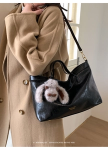 Close-up of black glossy oil wax leather tote bag with gold logo and plush charm