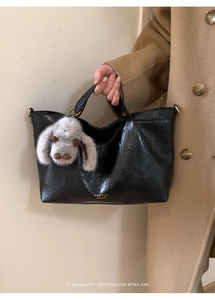 Detail of black faux leather tote bag with plush rabbit charm and gold logo lettering