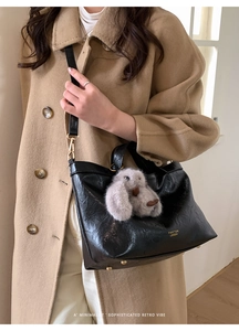 Detail view of a black glossy pleated tote bag with a cute plush rabbit charm