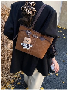 Close-up of brown suede tote bag with leather straps and bear charm in autumn setting