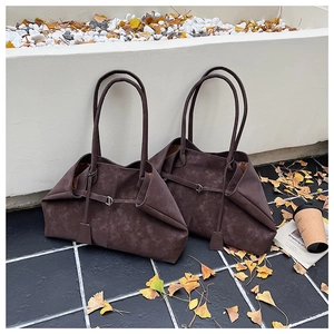 Detail of dark brown matte tote bag with slim handles and metal buckle on stone ground