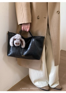 Detail of black leather tote bag with plush rabbit charm and gold logo lettering