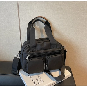 Detail of black multi-pocket crossbody bag with brown leather handles and wide strap