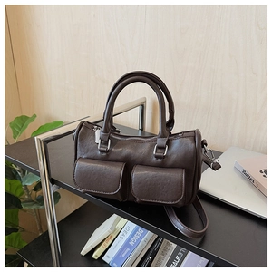 Detail of dark brown Boston bag with front flap pockets and silver hardware on a shelf