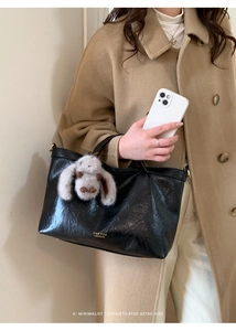 Detail of black glossy leather tote bag with golden logo and plush rabbit pendant decor