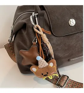 Detail of dark brown leather pillow bag with bear charm and woven wide strap