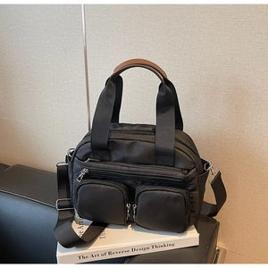 Detail of black nylon multi-pocket crossbody bag with brown leather handles and metal zippers