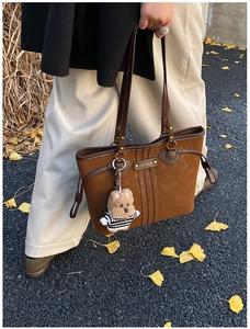 Détail du sac cabas en daim marron avec plaque logo dorée et breloque ours rayé
