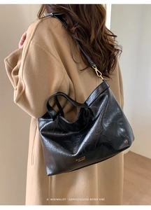 Detail of a vintage black leather tote bag with gold lettering on a camel wool coat