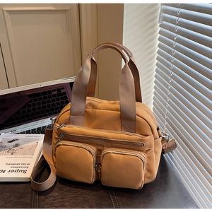 Detail of a ginger multi-pocket nylon shoulder bag on a desk with a laptop and books