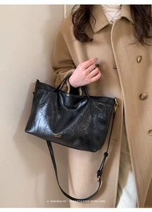 Detail of black vintage tote bag with glossy texture and golden hardware on camel coat