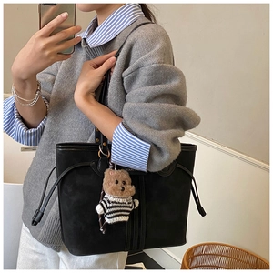 Close-up of black matte tote bag with side drawstrings and striped teddy bear charm