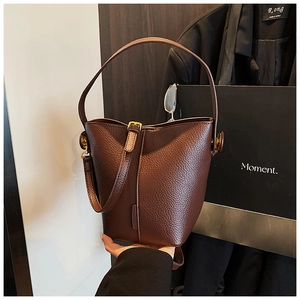 Detail of dark brown lychee leather bucket bag with metallic buckle and slim strap