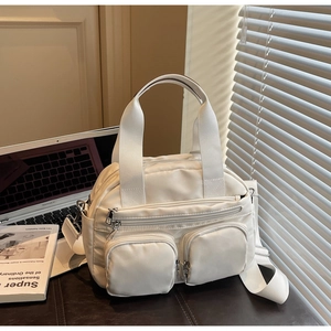 Close-up of white multi-pocket nylon crossbody bag with wide strap on office desk