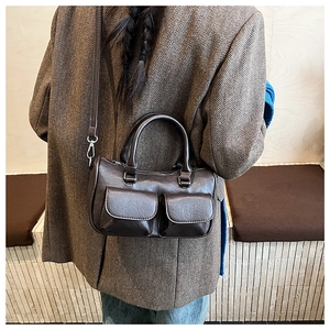 Detail of dark brown vintage faux leather handbag with functional front pockets on a model