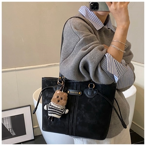 Close-up of black leather tote bag featuring metal brand logo and a cute bear charm