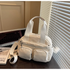 Detail of cream nylon crossbody bag with multiple front zip pockets on an office desk