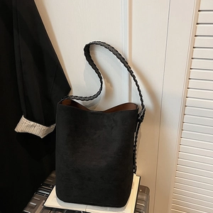 Detail of black suede bucket bag featuring woven shoulder strap and brown interior lining
