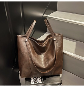 Dettaglio di una borsa tote marrone scuro con pelle testurizzata e rivetti metallici