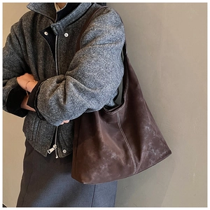 Detail of large brown suede hobo bag with white stitching on a gray suit model
