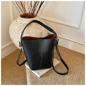 Detail of a black pebbled leather bucket bag with gold hardware and brown interior lining