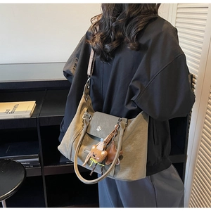 Detailed view of an olive green canvas tote bag with a bear charm and wide shoulder strap