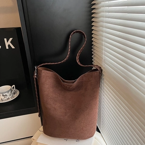 Detail of a brown suede bucket tote bag with woven shoulder straps and retro textures