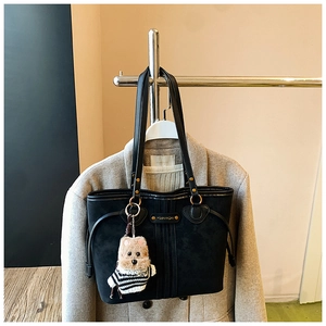 Détail du cabas noir mat avec pendentif chien en peluche sur fond de manteau en laine gris