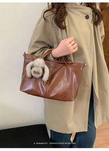 Brown leather tote bag featuring a cute plush animal charm in a minimalist retro style
