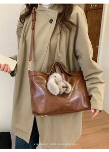 Brown leather tote bag detail with vintage texture and grey rabbit plush charm