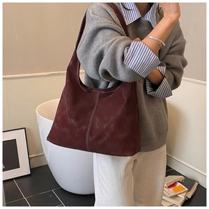 Detail of burgundy leather tote bag with white contrast stitching on model shoulder
