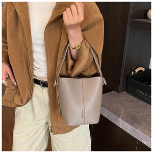 Close-up of taupe litchi grain leather bucket bag with circular hardware and top handle