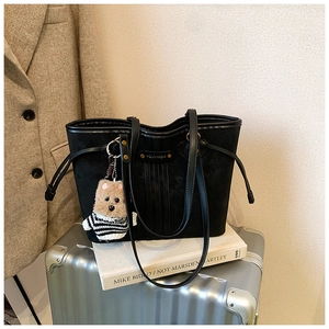 Détail d'un cabas noir mat avec plaque dorée et pendentif ours brun posé sur une valise