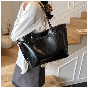 Macro shot of large black tote bag featuring studded side details and glossy leather texture