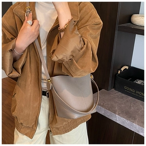 Detail of gray lychee leather bucket bag with gold buckle on a brown coat