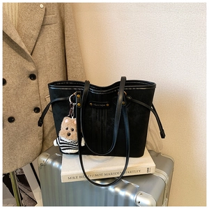 Détail d'un grand sac cabas noir avec un pendentif ours en peluche et logo métallique