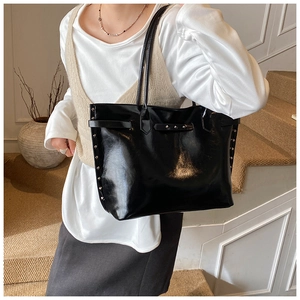 Close-up of black glossy tote bag with silver studs and polished patent leather finish