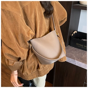 Macro shot of grainy taupe lychee leather bucket bag with adjustable strap and gold buckle