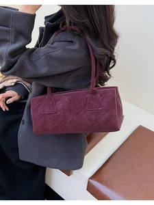 Détail d'un sac oreiller vintage bordeaux en cuir mat porté sur un manteau gris chiné