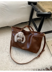 Detail of vintage brown oil wax leather bag with plush bunny charm and gold logo lettering