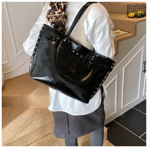 Detail of glossy black patent leather tote bag with silver rivets and buckle