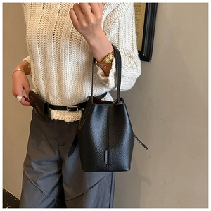 Detail of black pebbled leather bucket bag styled with a white knit sweater